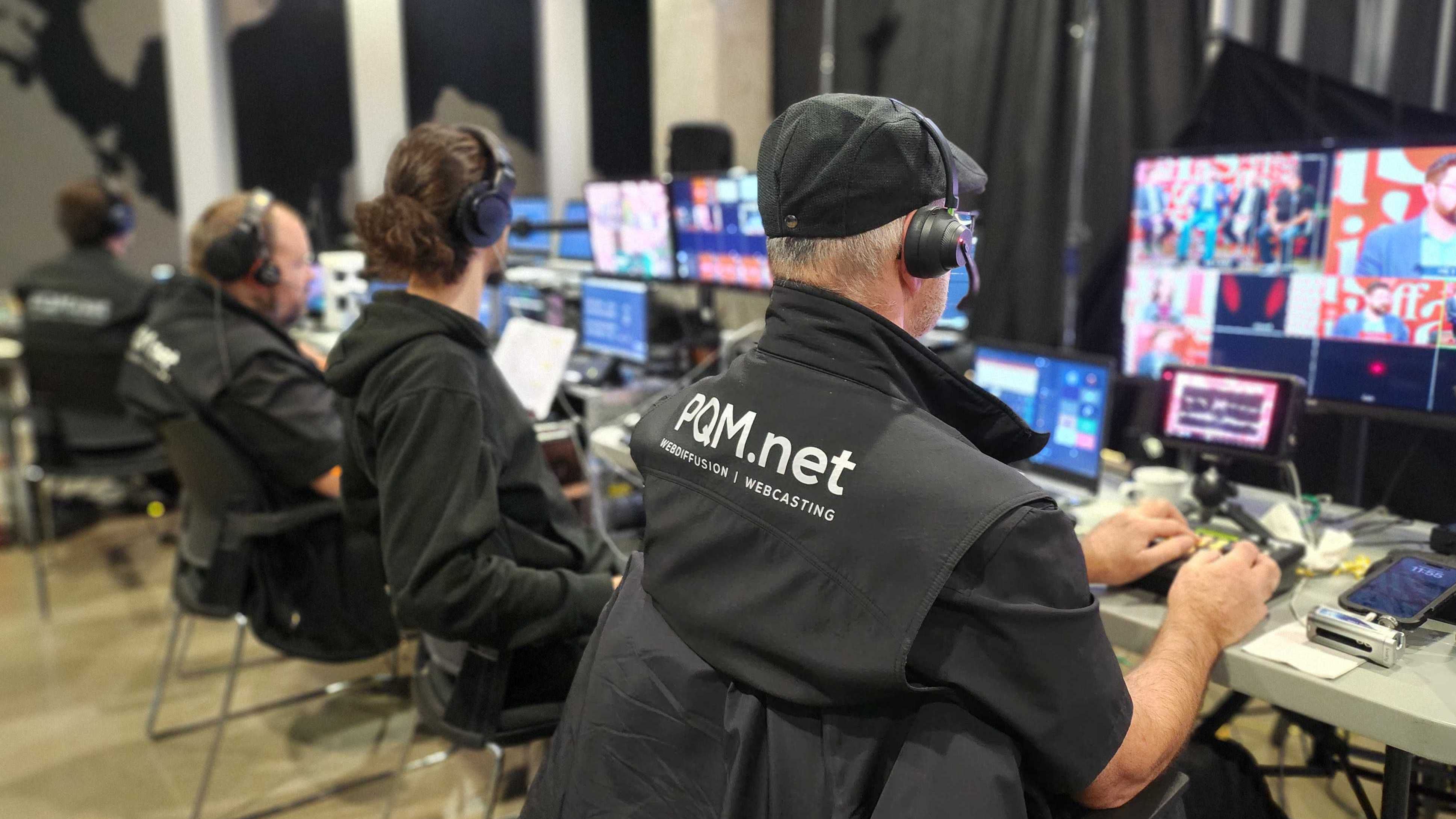 3 techniciens PQM.net, vu de dos, en show événementiel pour une webdiffusion. Écrans dans le background