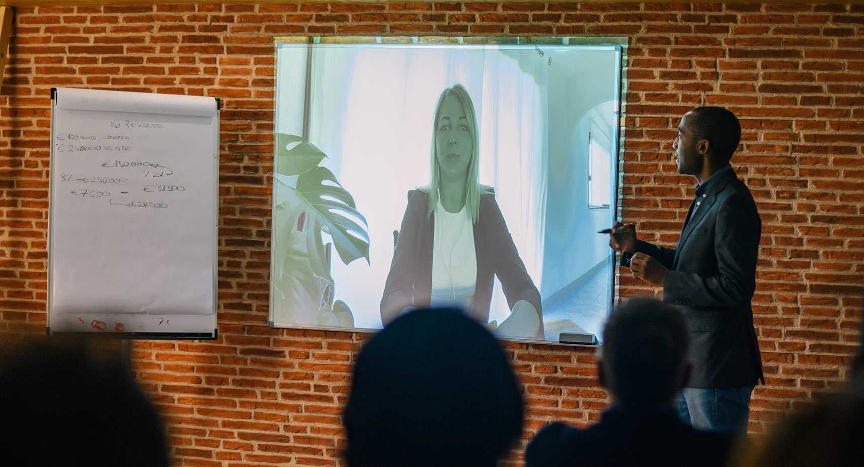 Personne de race noir qui est le porte parole d'un événement corporatif virtuel. Mur de brique et écran projecteur.